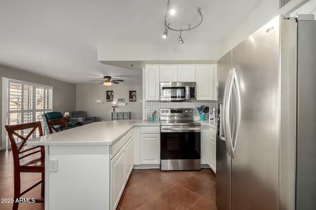 kitchen featuring stainless steel appliances, a peninsula, white cabinetry, light countertops, and backsplash