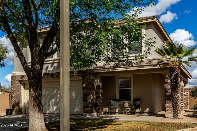 back of property featuring a garage, concrete driveway, brick siding, and stucco siding