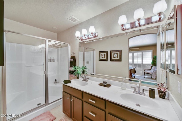 full bath with a stall shower, a textured ceiling, double vanity, and a textured wall