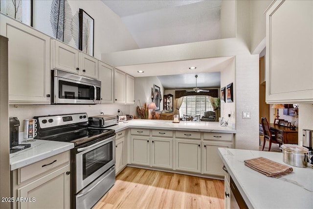 kitchen featuring stainless steel appliances, lofted ceiling, light wood finished floors, light stone countertops, and a ceiling fan