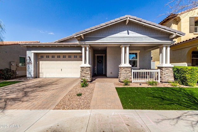 craftsman-style home with stucco siding, a tile roof, decorative driveway, a porch, and an attached garage