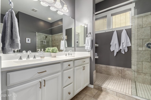 bathroom featuring visible vents, double vanity, a tile shower, tile patterned floors, and a sink