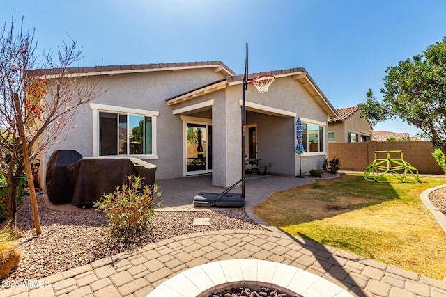 rear view of house featuring a patio area, stucco siding, fence, and an outdoor fire pit