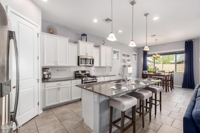 kitchen with visible vents, a sink, stainless steel appliances, a kitchen bar, and backsplash