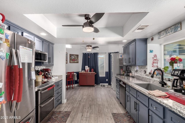 kitchen featuring a raised ceiling, light stone countertops, sink, and stainless steel appliances