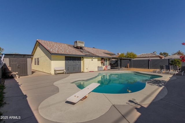 view of swimming pool featuring a diving board, a patio area, central AC, and a storage shed