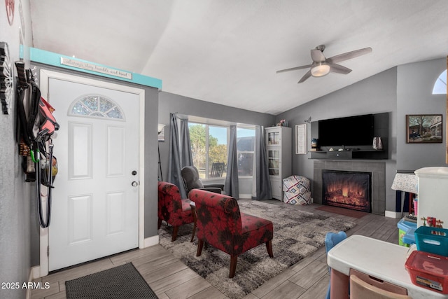 living room with ceiling fan, a tiled fireplace, and vaulted ceiling