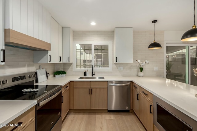 kitchen with tasteful backsplash, hanging light fixtures, stainless steel appliances, light countertops, and a sink