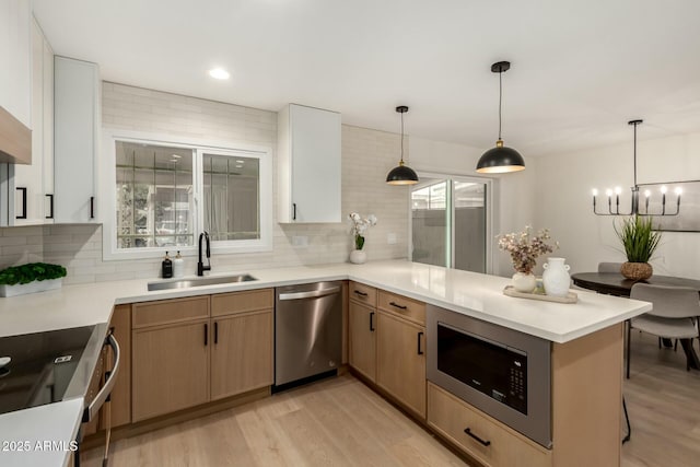 kitchen featuring a peninsula, a sink, light countertops, stainless steel dishwasher, and built in microwave