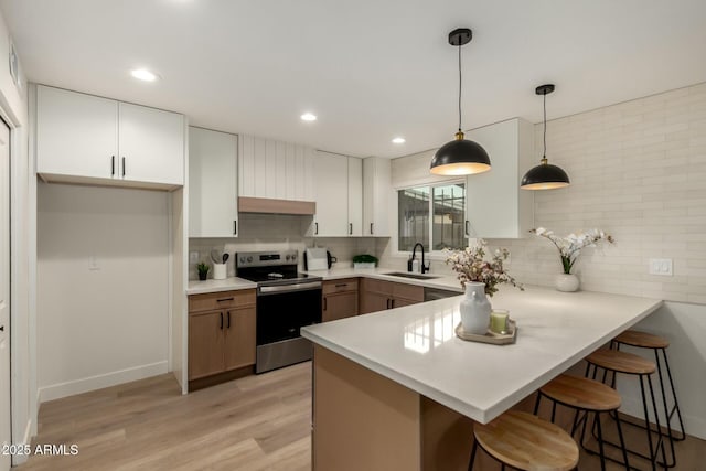 kitchen with light wood-style floors, a sink, stainless steel range with electric stovetop, a peninsula, and a kitchen bar