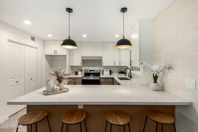 kitchen with electric range, a sink, visible vents, light countertops, and tasteful backsplash