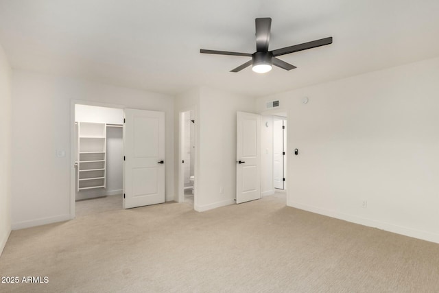 unfurnished bedroom with baseboards, visible vents, connected bathroom, light colored carpet, and a walk in closet