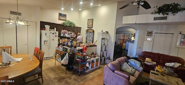 interior space featuring ceiling fan with notable chandelier, hanging light fixtures, white fridge with ice dispenser, light tile patterned floors, and dark brown cabinets