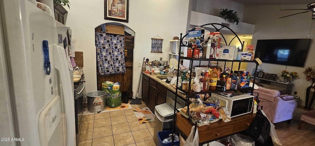 interior space featuring light tile patterned flooring, dark brown cabinetry, sink, ceiling fan, and white refrigerator with ice dispenser