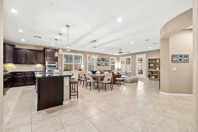 kitchen with an island with sink, a ceiling fan, visible vents, open floor plan, and a breakfast bar area