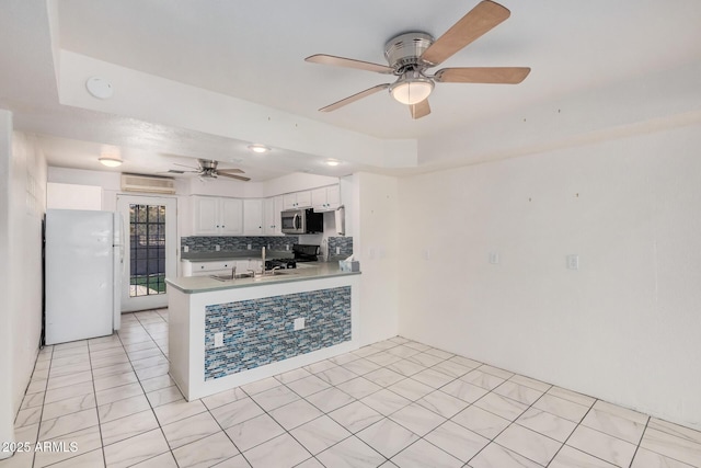 kitchen featuring ceiling fan, a sink, freestanding refrigerator, stainless steel microwave, and a peninsula
