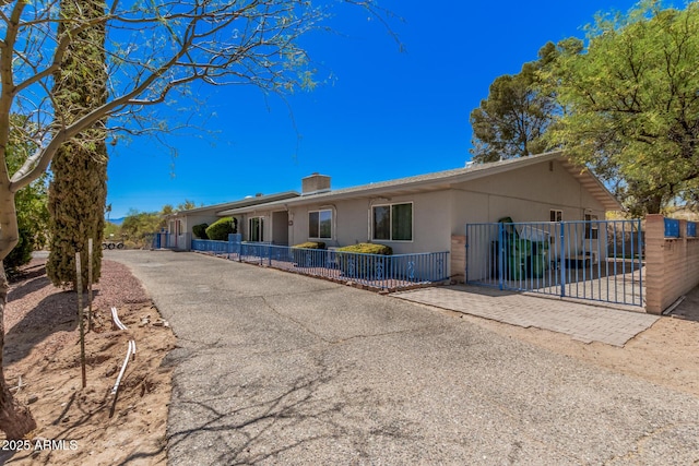 back of house featuring stucco siding, aphalt driveway, fence, and a chimney