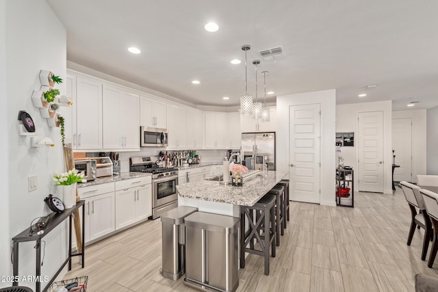 kitchen featuring white cabinets, backsplash, stainless steel appliances, and an island with sink