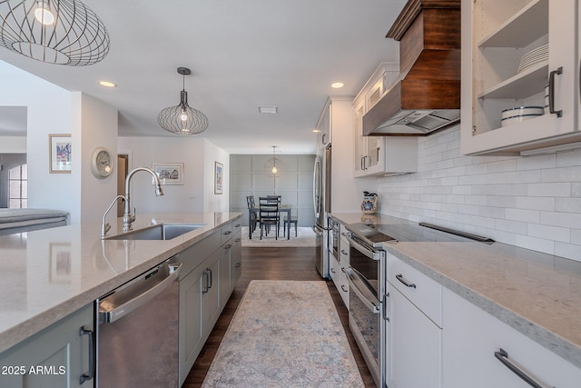 kitchen with glass insert cabinets, dark wood-style floors, custom range hood, a sink, and appliances with stainless steel finishes