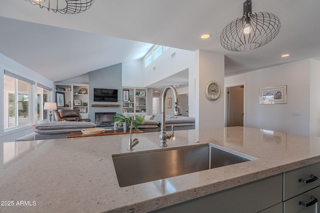 kitchen with a glass covered fireplace, gray cabinets, light stone counters, a sink, and vaulted ceiling