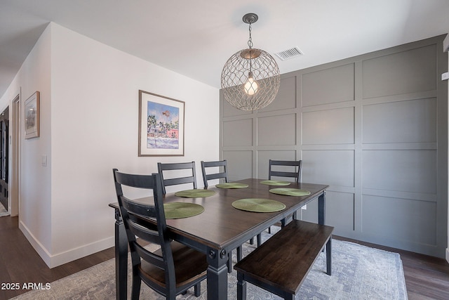 dining room featuring baseboards, visible vents, dark wood finished floors, and a decorative wall