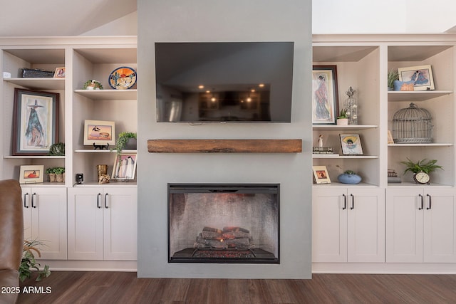 living room with dark wood-type flooring, a glass covered fireplace, and built in shelves