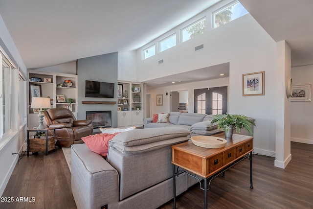 living room featuring visible vents, dark wood finished floors, baseboards, high vaulted ceiling, and a glass covered fireplace