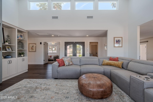 living room with visible vents, dark wood-type flooring, a towering ceiling, and french doors