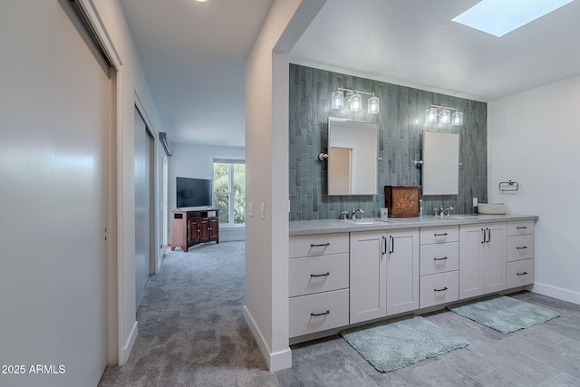 full bathroom featuring a skylight, baseboards, double vanity, and a sink