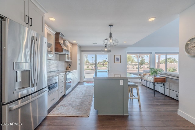 kitchen with a kitchen island with sink, tasteful backsplash, dark wood finished floors, stainless steel fridge with ice dispenser, and premium range hood