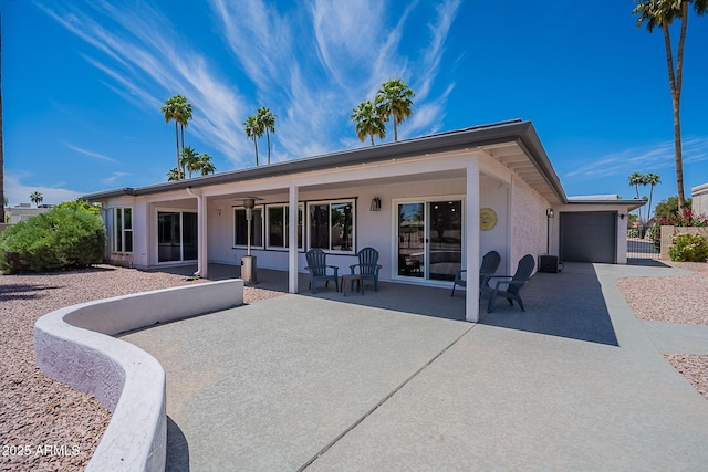rear view of house with a garage, stucco siding, concrete driveway, and a patio area