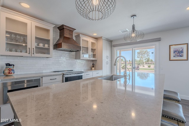 kitchen with visible vents, a sink, light stone countertops, premium range hood, and electric stove
