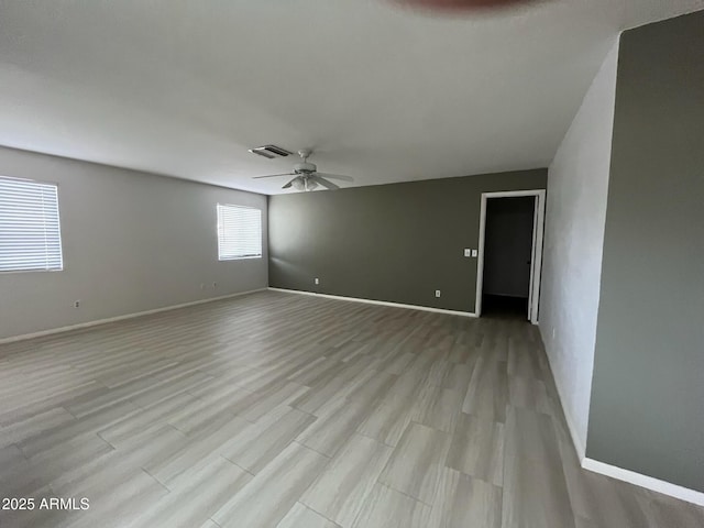 unfurnished room with a ceiling fan, visible vents, light wood-style floors, and baseboards