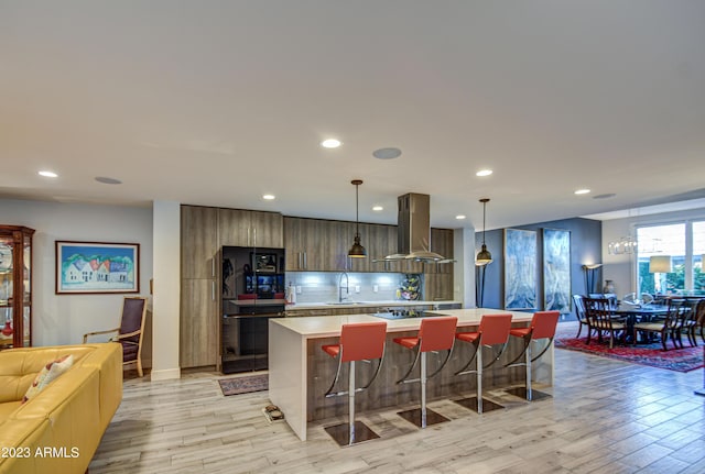 kitchen featuring pendant lighting, island range hood, sink, a breakfast bar area, and a center island