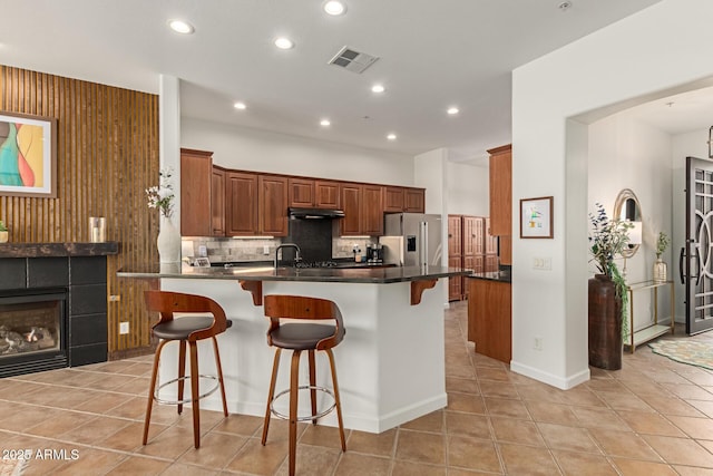 kitchen featuring a tile fireplace, stainless steel fridge, light tile patterned floors, kitchen peninsula, and a breakfast bar area