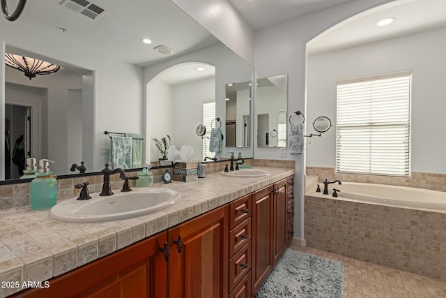 bathroom featuring tile patterned floors, vanity, and a relaxing tiled tub