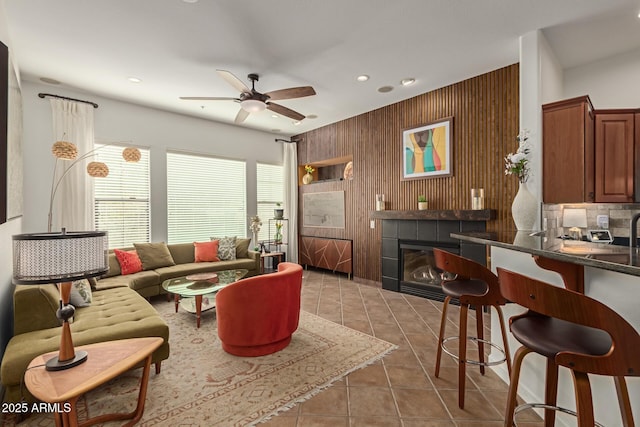 tiled living room with a fireplace, ceiling fan, and wooden walls