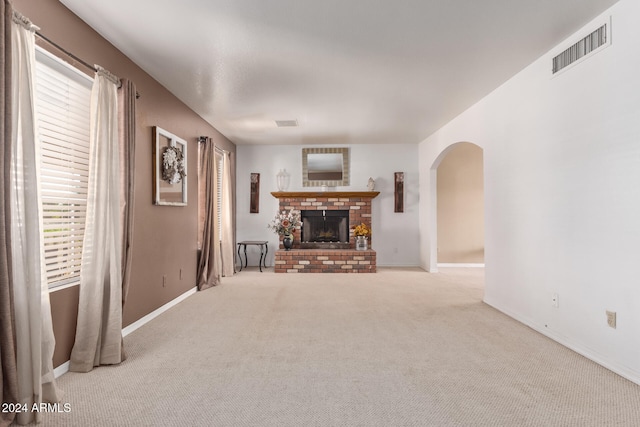 unfurnished living room with a healthy amount of sunlight, light colored carpet, and a brick fireplace