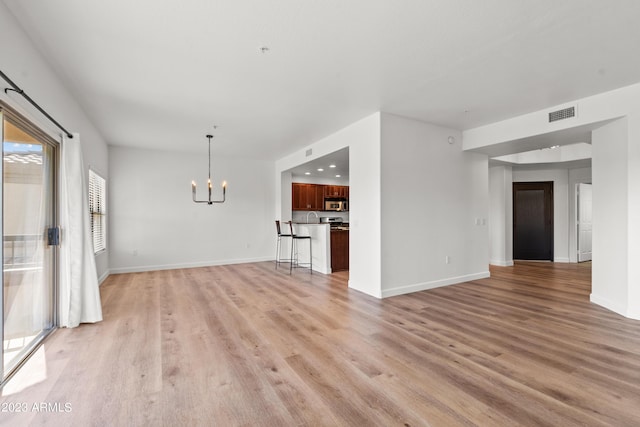 unfurnished living room with light wood-style floors, visible vents, baseboards, and an inviting chandelier