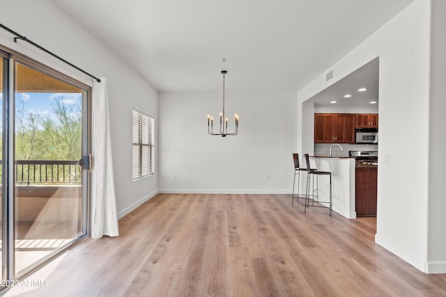 unfurnished dining area featuring light wood-style floors, baseboards, a chandelier, and a sink