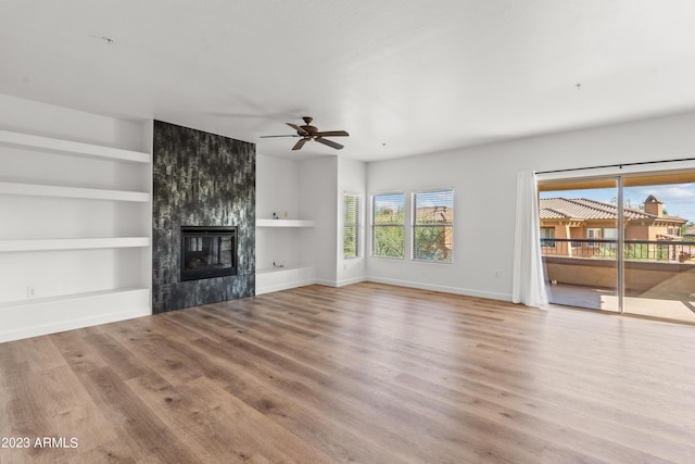 unfurnished living room featuring ceiling fan, baseboards, built in features, light wood-style floors, and a tiled fireplace