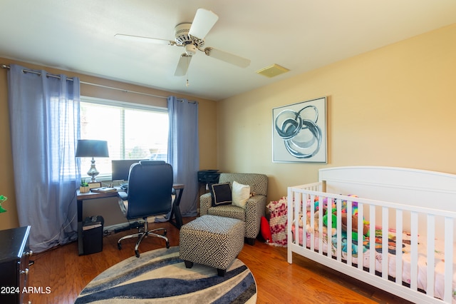 bedroom featuring wood-type flooring, a nursery area, and ceiling fan