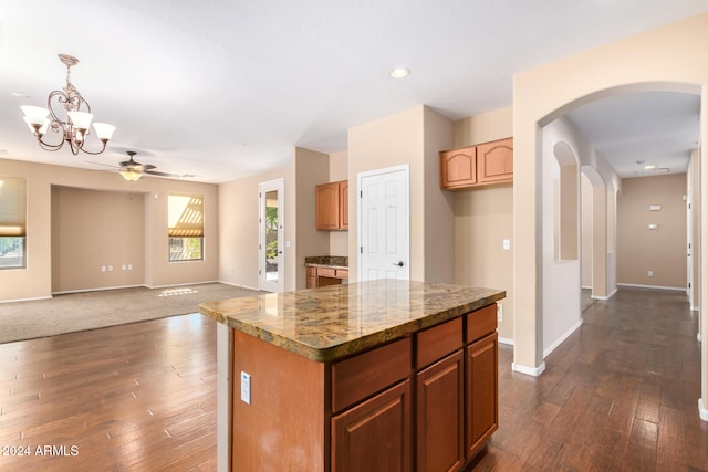 kitchen featuring light stone counters, dark hardwood / wood-style floors, ceiling fan with notable chandelier, hanging light fixtures, and a center island