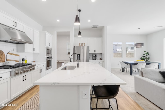 kitchen featuring appliances with stainless steel finishes, decorative light fixtures, sink, and a center island with sink