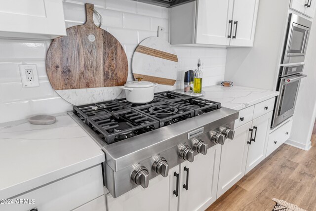 kitchen featuring light hardwood / wood-style floors, stainless steel appliances, light stone counters, and white cabinets