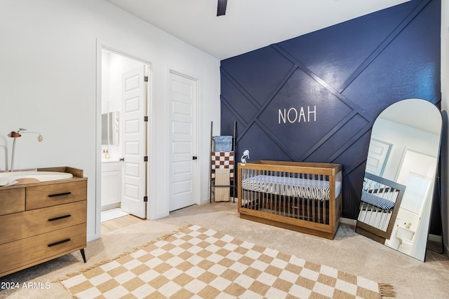 carpeted bedroom featuring ceiling fan, ensuite bathroom, and a nursery area