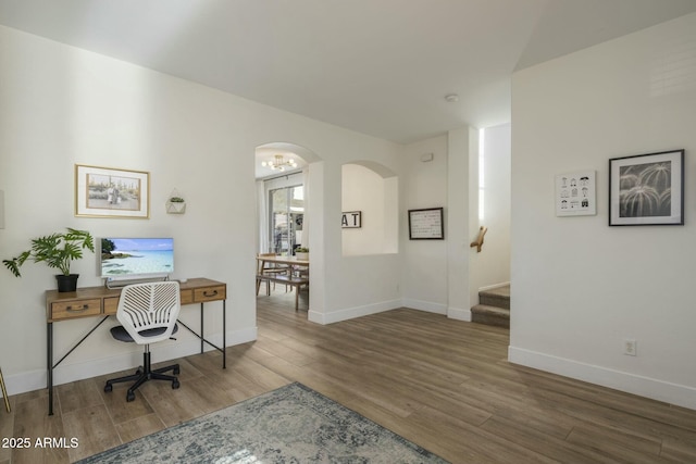 office space featuring arched walkways, baseboards, and wood finished floors