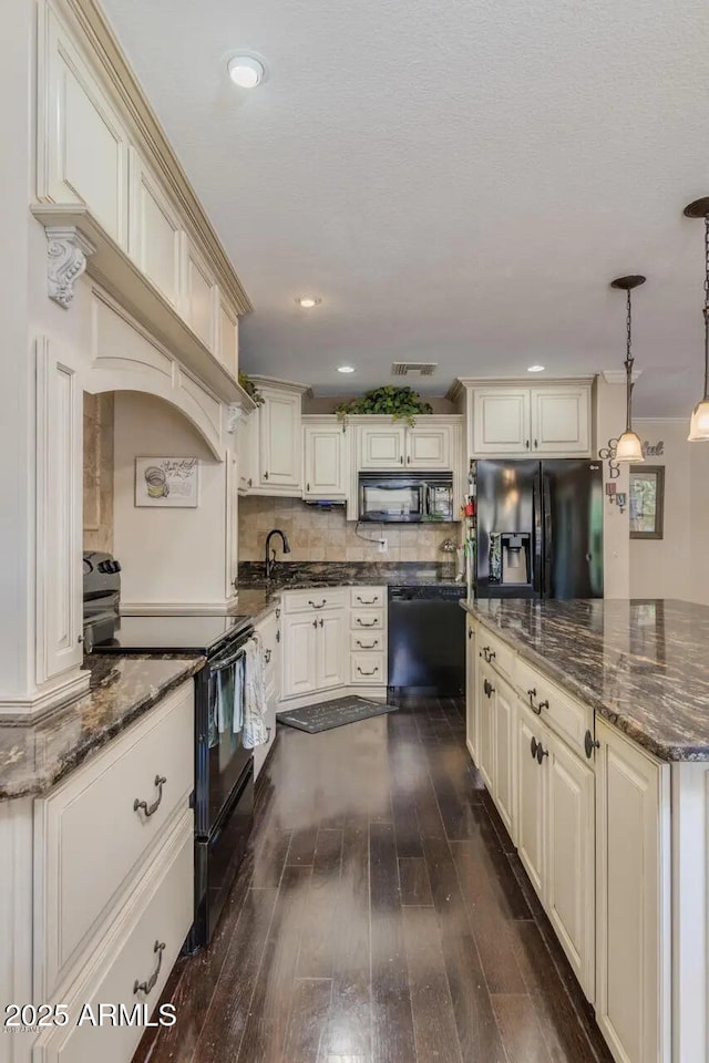 kitchen featuring dark stone counters, dark wood-style flooring, black appliances, cream cabinets, and backsplash