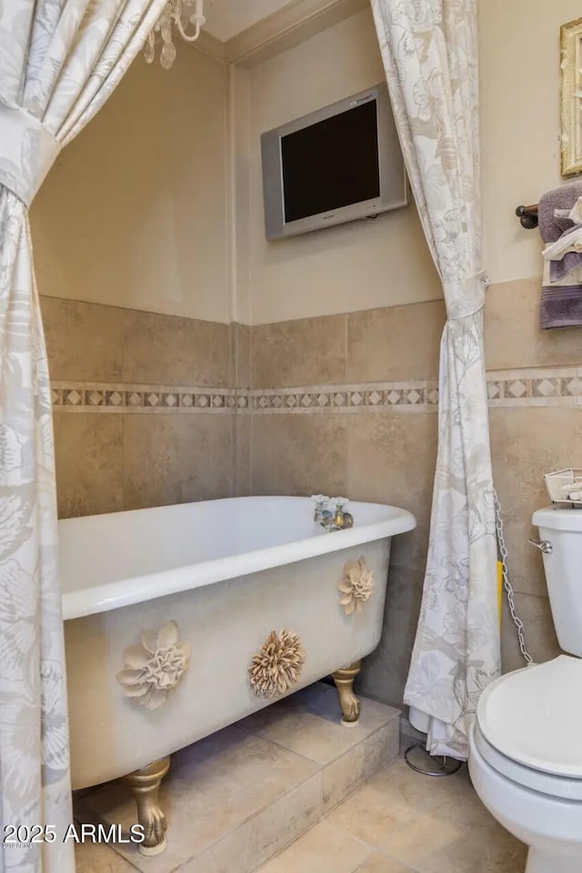 full bathroom with toilet, wainscoting, tile patterned floors, a soaking tub, and tile walls