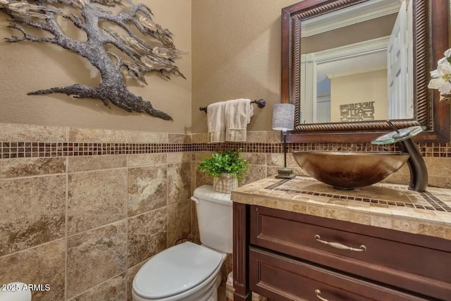 half bath featuring a wainscoted wall, toilet, tile walls, and vanity